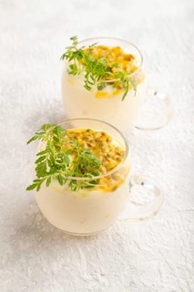 Yogurt with passionfruit and marigold microgreen in glass on gray concrete background. Side view,