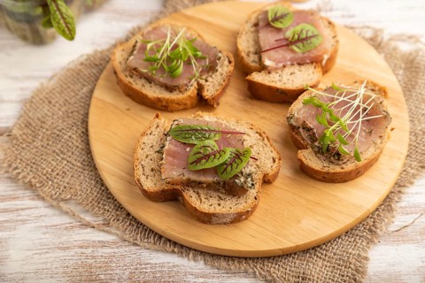 Bread sandwiches with jerky salted meat, sorrel and cilantro microgreen on white wooden background