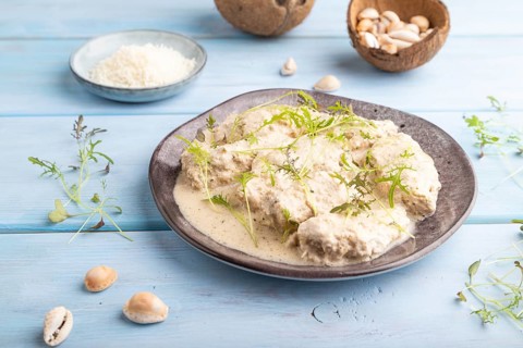 Stewed chicken fillets with coconut milk sauce and mizuna cabbage microgreen on blue wooden