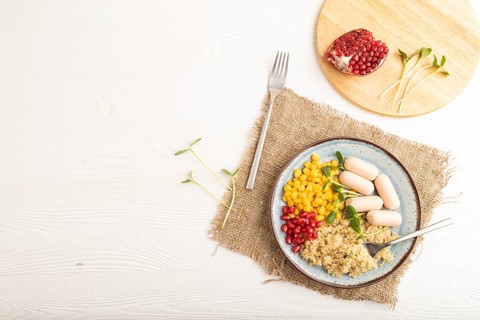 Mixed quinoa porridge, sweet corn, pomegranate seeds and small sausages on white wooden background.
