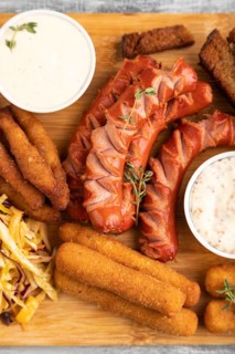 Set of snacks: sausages, nuggets, cheese sticks, toast, cabbage salad on a cutting board on a gray