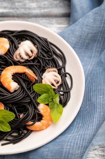 Black cuttlefish ink pasta with shrimps or prawns and small octopuses on gray wooden background and