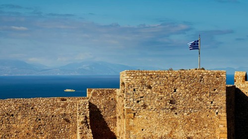 Historic fortress walls under a partly cloudy sky with Greek flag and sea view, Chlemoutsi, High