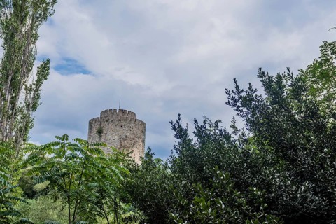 Tower of castle ruins behind treeline against blue partly cloudy sky in Istanbul, Tuerkiye