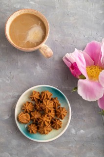 Homemade soft caramel fudge candies on blue plate and cup of coffee on gray concrete background,