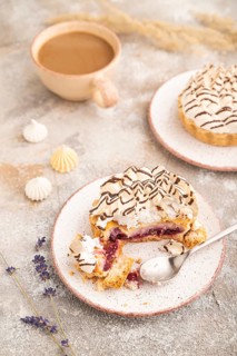 Two tartlets with meringue cream and cup of coffee on brown concrete background. side view,