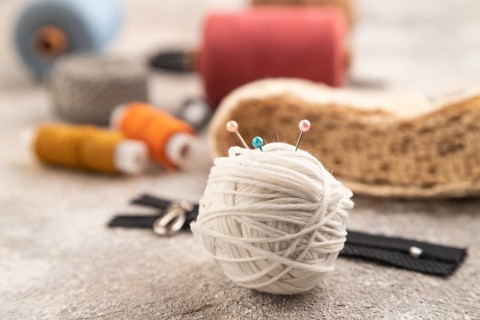 Sewing accessories: scissors, thread, thimbles, braid on brown concrete background. Side view,