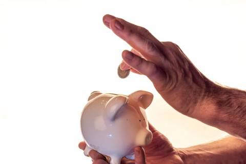 Hand of a man holding a white piggy bank and putting a coin into it, white background, studio shot,