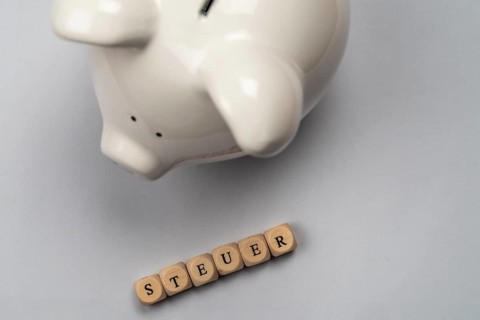 White piggy bank and tax lettering against a white background, top view, studio shot, Germany,