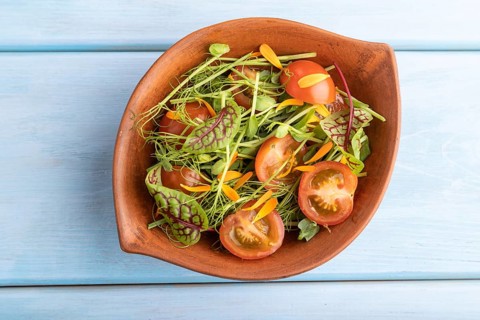 Vegetarian vegetables salad of tomatoes, marigold petals, microgreen sprouts on blue wooden