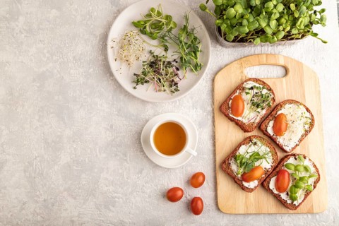 Red beet bread sandwiches with cream cheese, tomatoes and microgreen on gray concrete background.