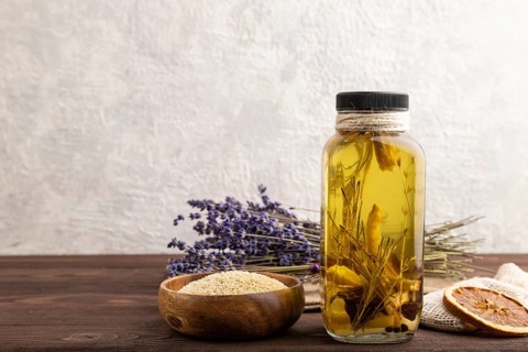 Sunflower oil in a glass jar with various herbs and spices, lavender, sesame, rosemary on a brown