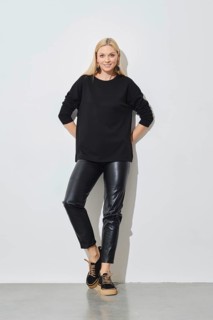 Smiling woman in black pullover and leather trousers leaning against white wall