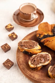 Homemade sweet bun with chocolate cream and cup of coffee on a gray concrete background and linen