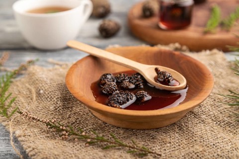 Pine cone jam with herbal tea on gray wooden background and linen textile. Side view, close up,