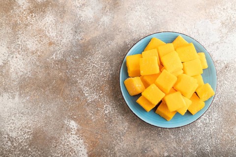 Dried and candied mango cubes on blue plate on brown concrete background. Top view, flat lay, copy