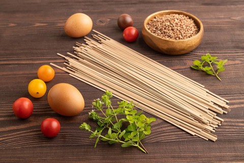 Japanese buckwheat soba noodles with tomato, eggs, spices, herbs on brown wooden background. Side