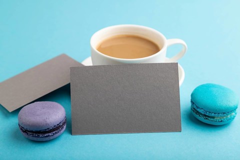 Gray paper business card mockup with blue and violet macaroons and cup of coffee on blue pastel