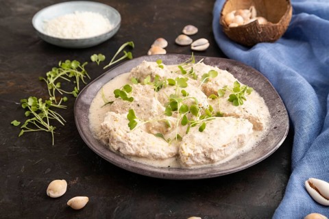 Stewed chicken fillets with coconut milk sauce and rucola microgreen on black concrete background