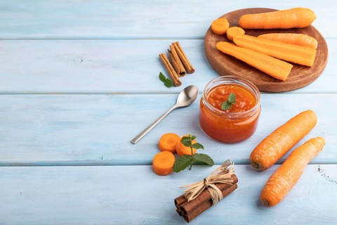 Carrot jam with cinnamon in glass jar on blue wooden background. Side view, copy space