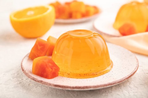 Papaya and orange jelly on gray concrete background and orange linen textile. side view, flat lay,