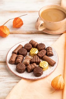 Chocolate candies with cup of coffee and physalis flowers on a white wooden background and orange