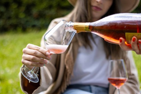 Unrecognizable woman holding a glass cup while being served some red champagne outdoors in the park