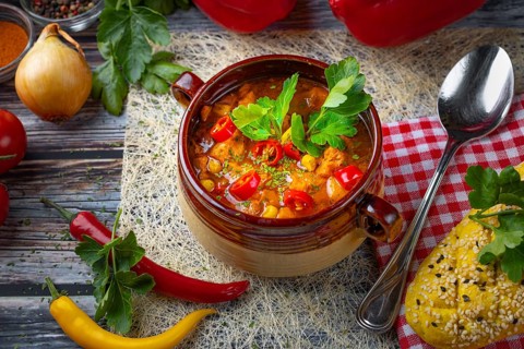 Colourful goulash soup in a ceramic cup, decorated with parsley, surrounded by ingredients