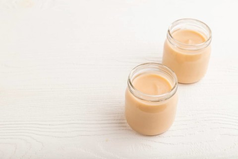 Baby puree with fruits mix, apple, banana infant formula in glass jar on white wooden background.
