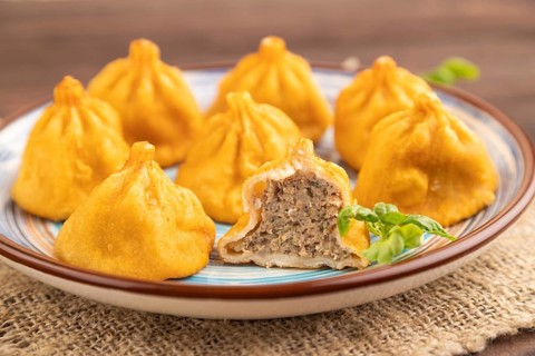 Fried manti dumplings with pepper, basil on brown wooden background and linen textile. Side view,