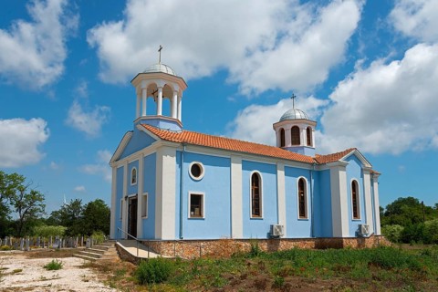 A small church with blue walls and white domes under a clear blue sky surrounded by nature, Sveti