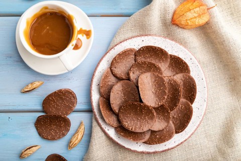 Chocolate chips with cup of coffee and caramel on a blue wooden background and linen textile. top