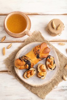 Homemade sweet bun with honey almonds and cup of green tea on a white wooden background and linen