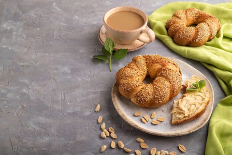 Homemade sweet bun with peanut butter and cup of coffee on a gray concrete background and green