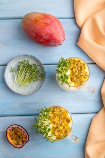 Mango yogurt with passionfruit and cilantro microgreen in glass on blue wooden background with