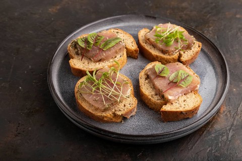 Bread sandwiches with jerky salted meat, sorrel and cilantro microgreen on black concrete