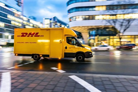 Vehicle of the parcel service provider DHL, modern architecture of the city centre in the evening,