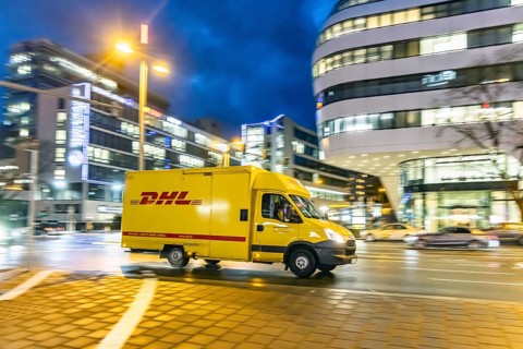 Vehicle of the parcel service provider DHL, modern architecture in the evening, motion blur,