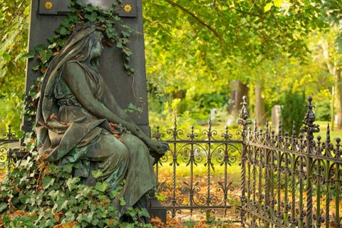 Sculpture of a mourning woman with green patina in a cemetery in autumn, detail of a green