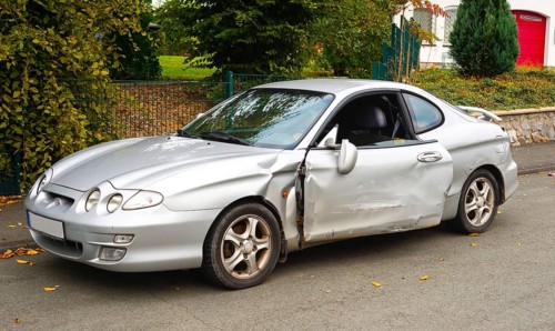 Accident car, sporty car with accident damage standing on a road, silver motor vehicle, car with