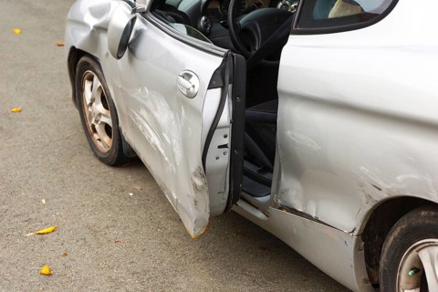 Accident car, sporty car with accident damage standing on a road, damaged, open door, silver motor