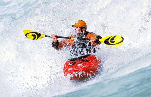 A kayaker rides in the spray in a wave in the Isar at the Wittelsbacherbrücke, Munich, Bavaria,
