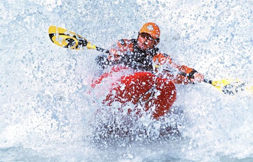 A kayaker rides in the spray in a wave in the Isar at the Wittelsbacherbrücke, Munich, Bavaria,