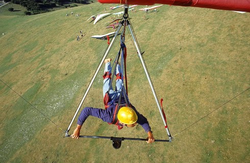 Pilot's perspective, a young man hangs in a hang glider and flies over the launch site, where other