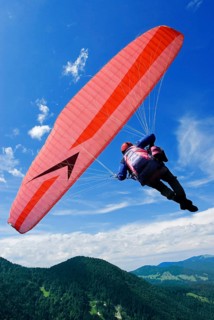 A man hangs in a red and white paraglider high above the meadows near Lenggries, pilot's