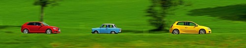A red and a yellow car drive quickly through the green meadow landscape, a Trabant, also known as a