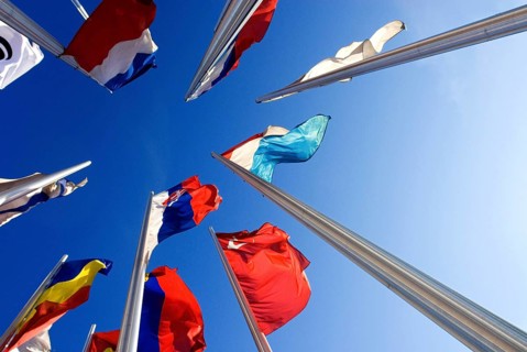Wide angle shot of European national flags, frog perspective, against blue sky, in front of the