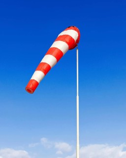 A red and white windsock blows in a light breeze against a blue sky