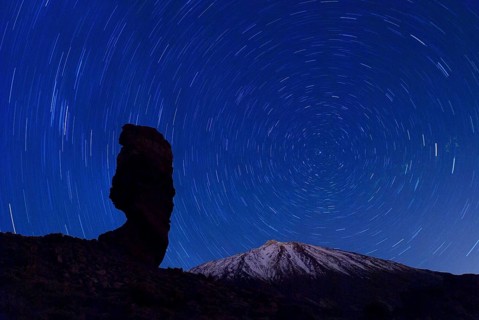 The Roque Cinchado at night with circling stars in the clear night sky and the summit of Pico de