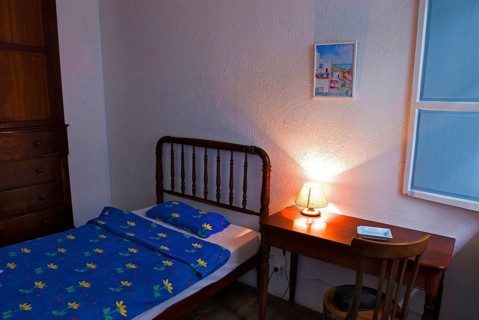 Bed and wooden table with illuminated bedside lamp in the room of a small, simple hotel or